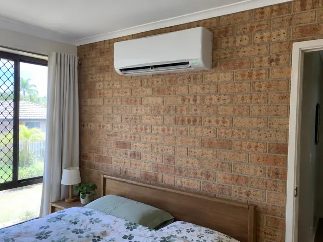 Wall-mounted split system above a bed in a brick bedroom with curtains and window in Highland Park