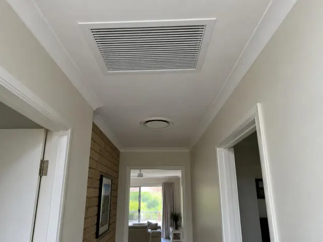 Ceiling return-air grille and round outlet in a hallway with white trim and brick feature wall in Worongary