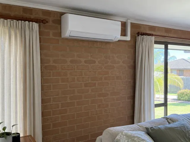 Wall-mounted split system above curtains on a brick interior wall in a home in Carrara